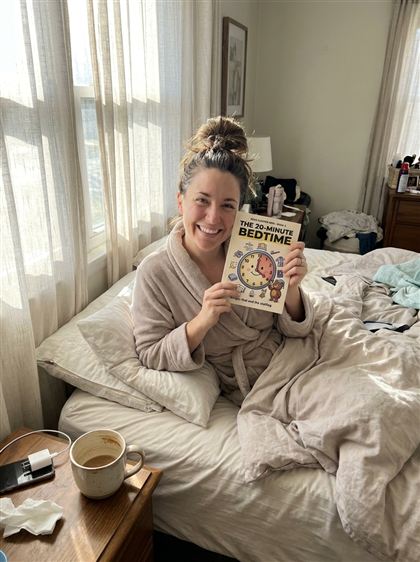 Well-rested mom in her own bed holding Book 2